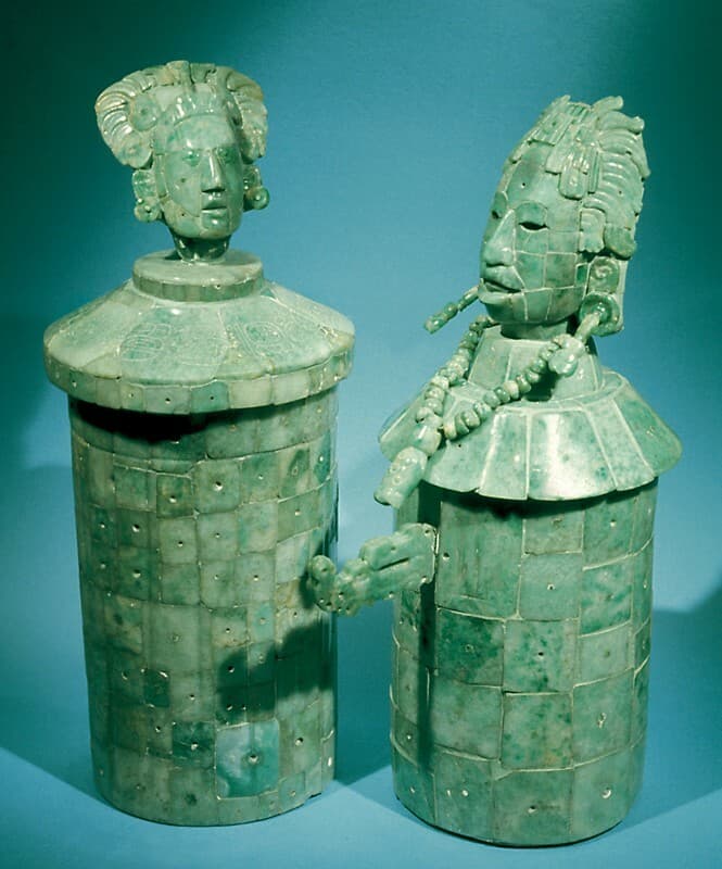 The image shows two jade artifacts - a lidded jar and a figurative sculpture. The figures are carved with intricate geometric patterns in the distinctive green hue of jade. The artifacts exhibit the material's natural markings and textures.